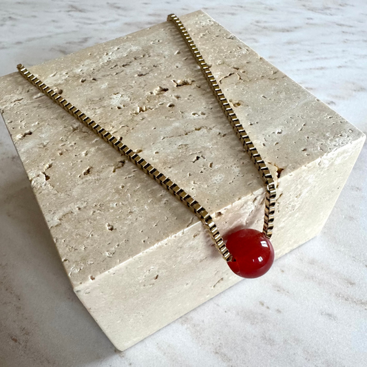 Golden Necklace with Red Agate Pendant Ball on beige stone display