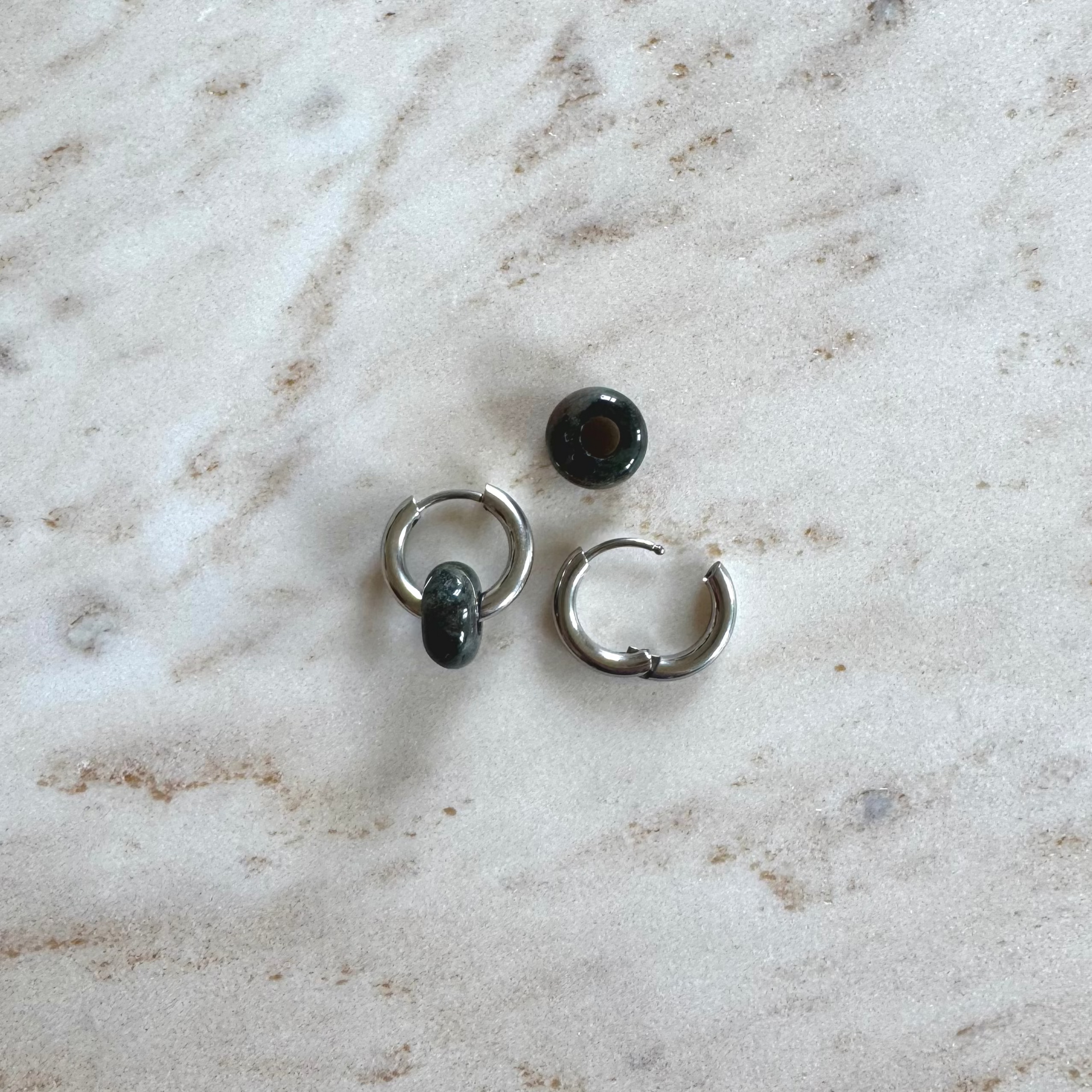 Two silvery hoop earrings on  with 2 green agate donut pendants on beige marble