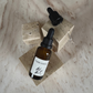 Ritual Oil Forgiveness in brown bottle and dropper on beige stone display