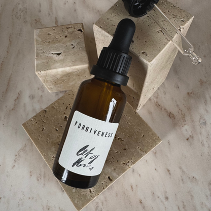 Ritual Oil Forgiveness in brown bottle and dropper on beige stone display