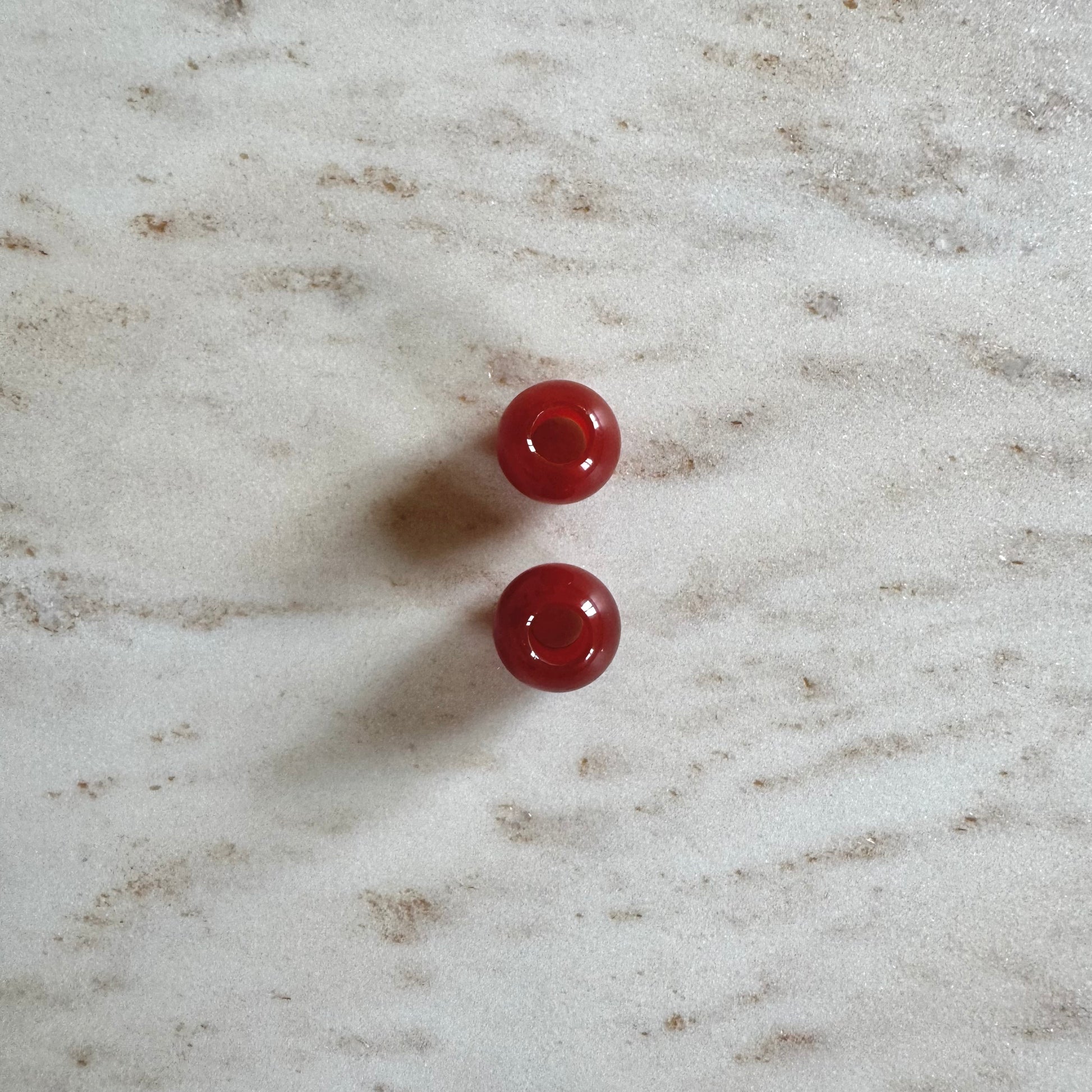 2 rote Achat Anhänger Ballform auf weissem Marmor Stein