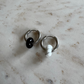 Two silvery hoop earrings on top of each other with 1 black and 1 white donut pendants on beige marble