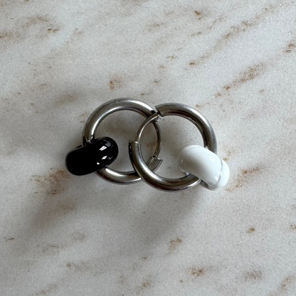 Two silvery hoop earrings on top of each other with 1 black and 1 white donut pendants on beige marble