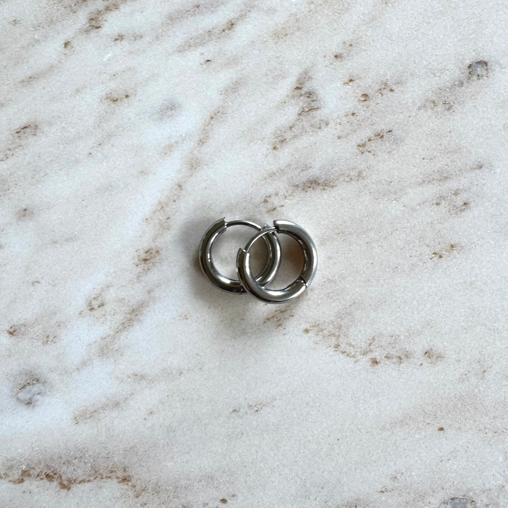 Two silvery hoop earrings on top of each on beige marble